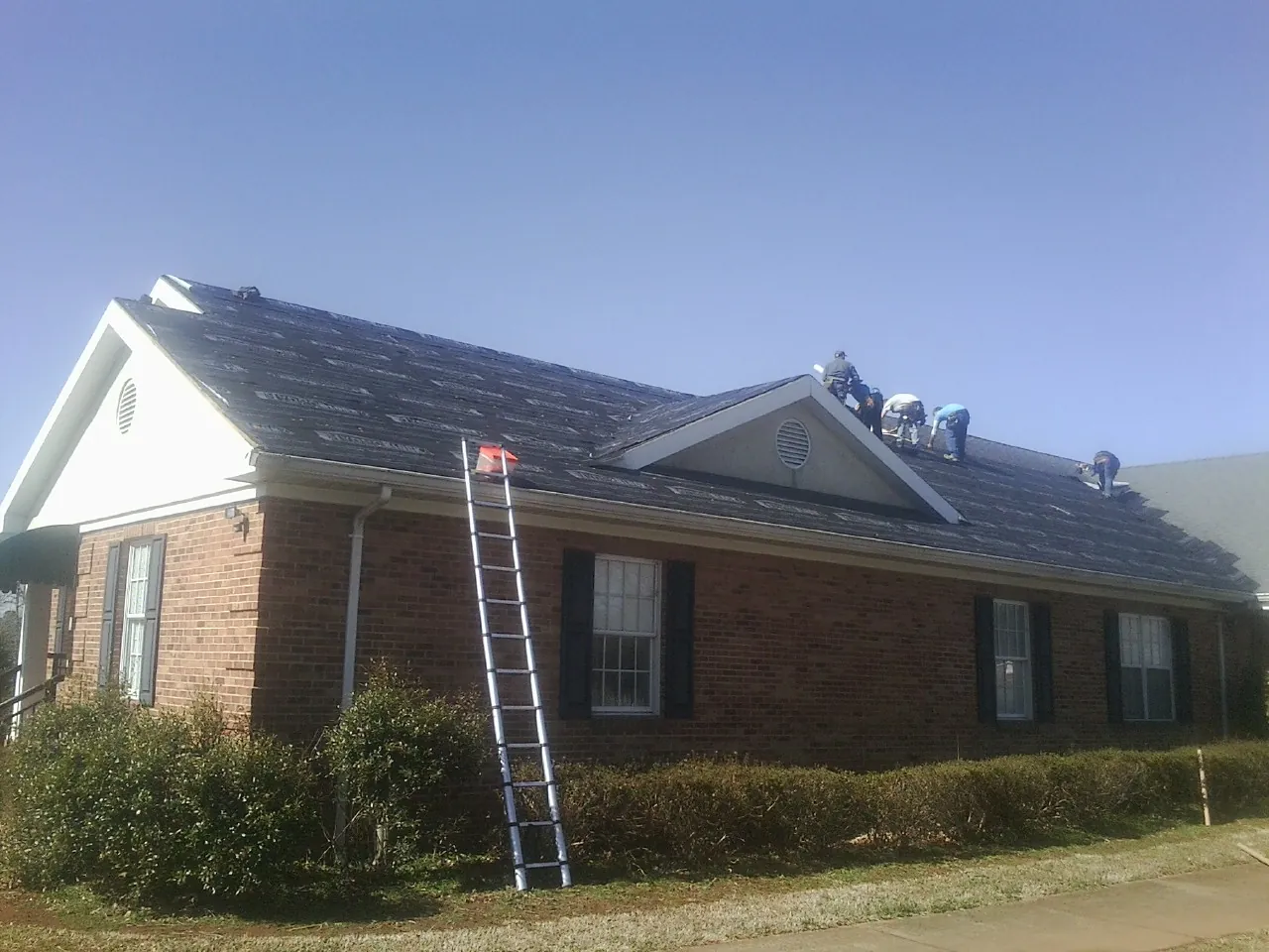 Crew tearing shingles off a brick ranch roof with a ladder set — Metal Roof Repair work by our crew in Carol Stream