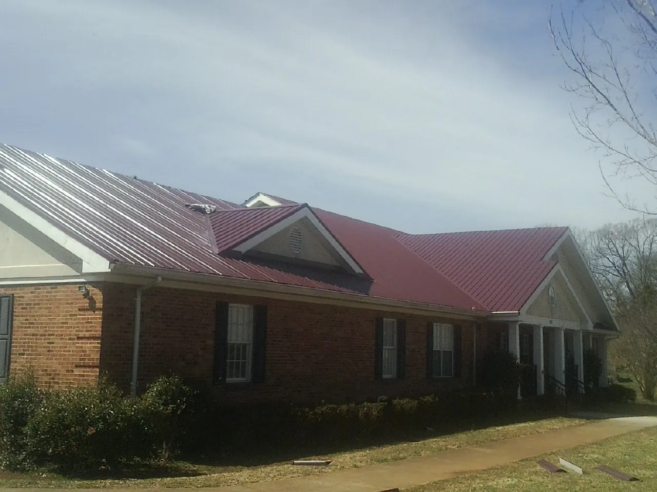 Red metal roof with gabled entries on a long brick building, from a Hail Damage Roof Repair job in Carol Stream