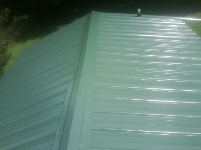 New green metal panels meeting at the ridge of a roof — Flat Roof Repair work by our crew in Carol Stream