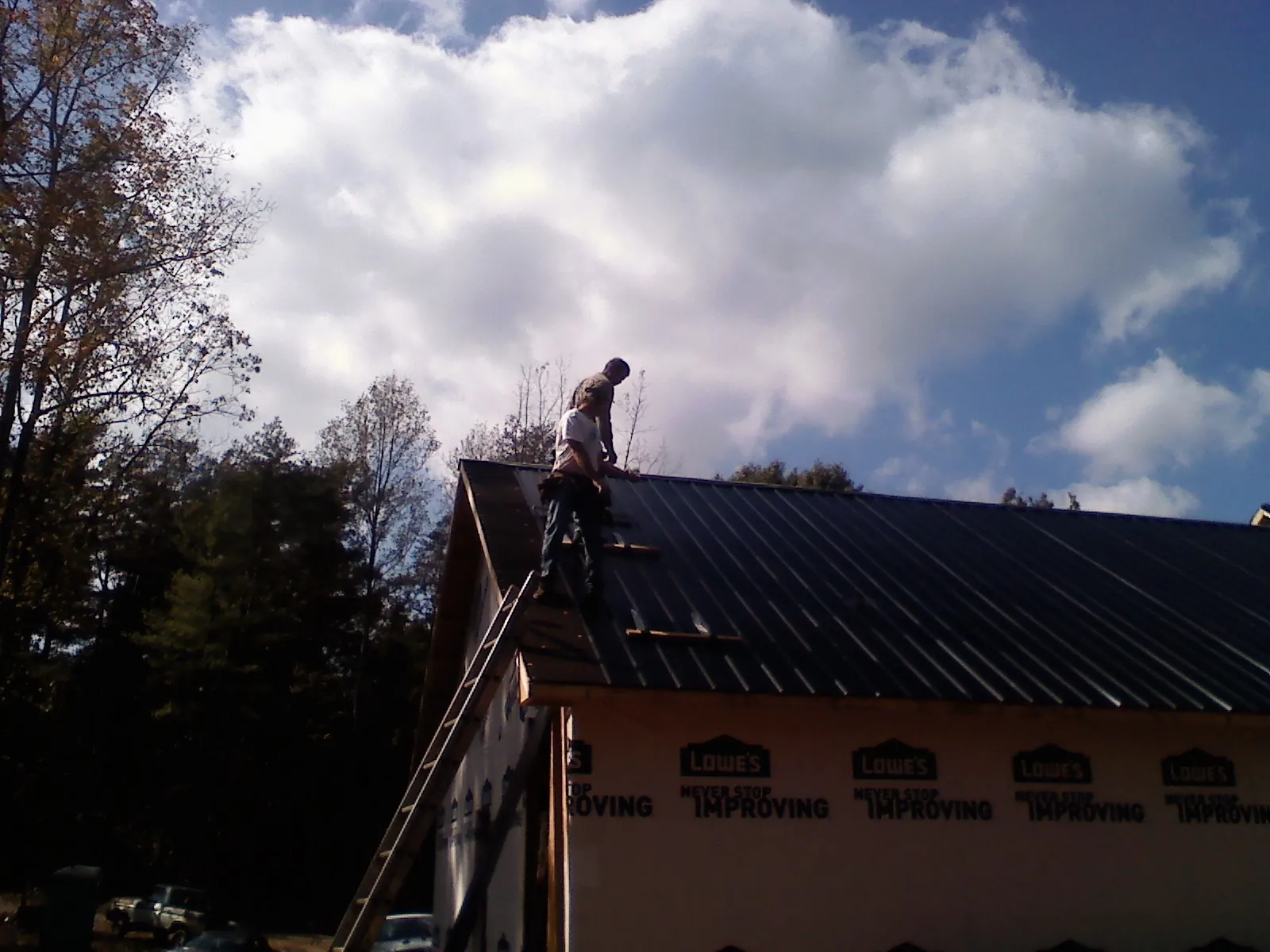 Roofer fastening dark metal panels high against a cloudy sky, from a Roof Inspection job in Carol Stream